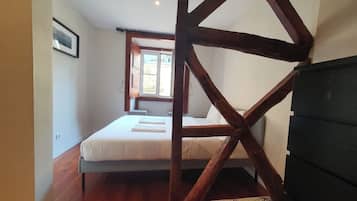 A bedroom with a wooden truss ceiling, a bed with white bedding, and a window providing natural light.