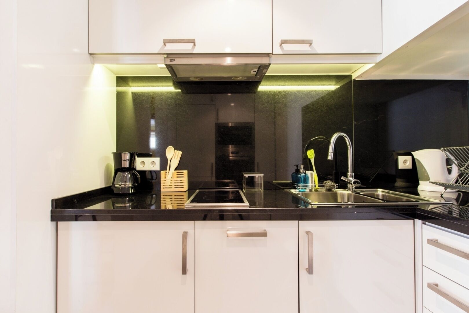 Une cuisine moderne avec des meubles blancs, un plan de travail noir et des appareils en acier inoxydable.