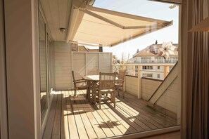 A balcony with a table and chairs, a retractable awning, and a view of buildings in the background. - Sunny Duplex Stay in City Center (Knokke-Heist)