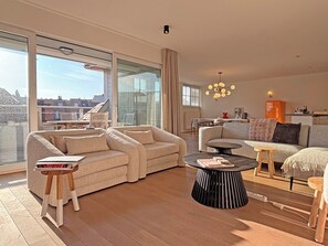 A modern living room with a sofa, a coffee table, and a dining area with a table and chairs. - Sunny Duplex Stay in City Center (Knokke-Heist)