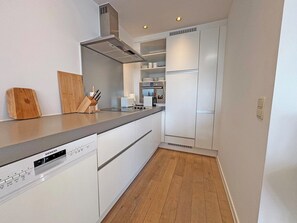 A modern kitchen with white cabinetry, a stainless steel range hood, and a built-in dishwasher. - Sunny Duplex Stay in City Center (Knokke-Heist)