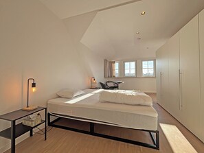 Een moderne slaapkamer met een bed, nachtkastjes, een bureau en een kledingkast.