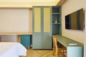 Quarto de hotel com cama, escrivaninha, guarda-roupa e televisão.