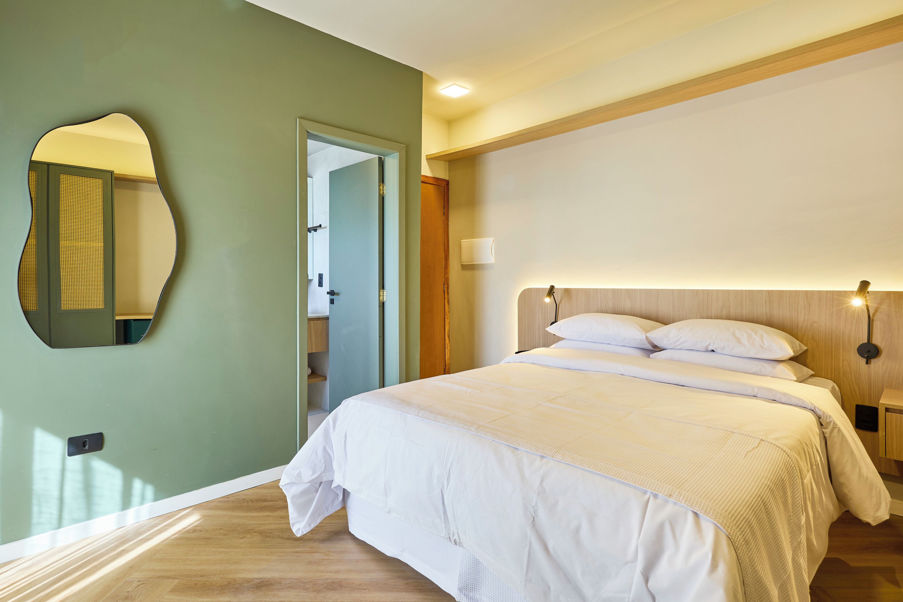 A bedroom with a bed, a mirror, a door, and a nightstand with a lamp.