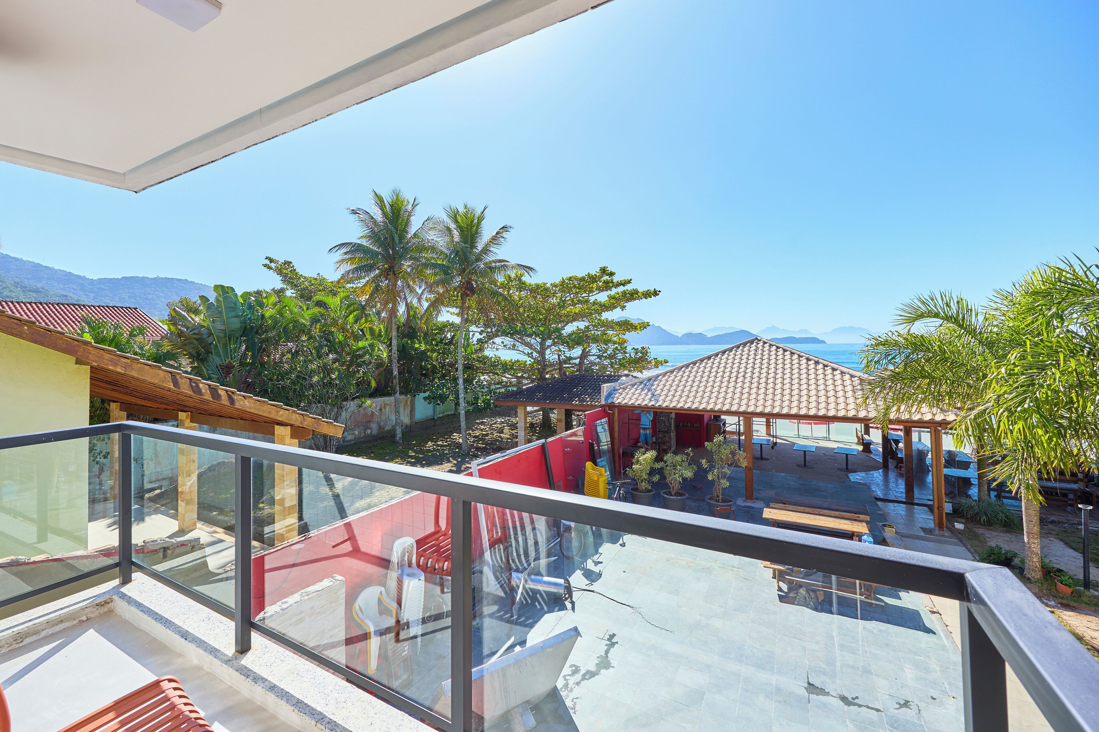 A balcony with a glass railing overlooking a patio area with outdoor seating and a view of the sea.