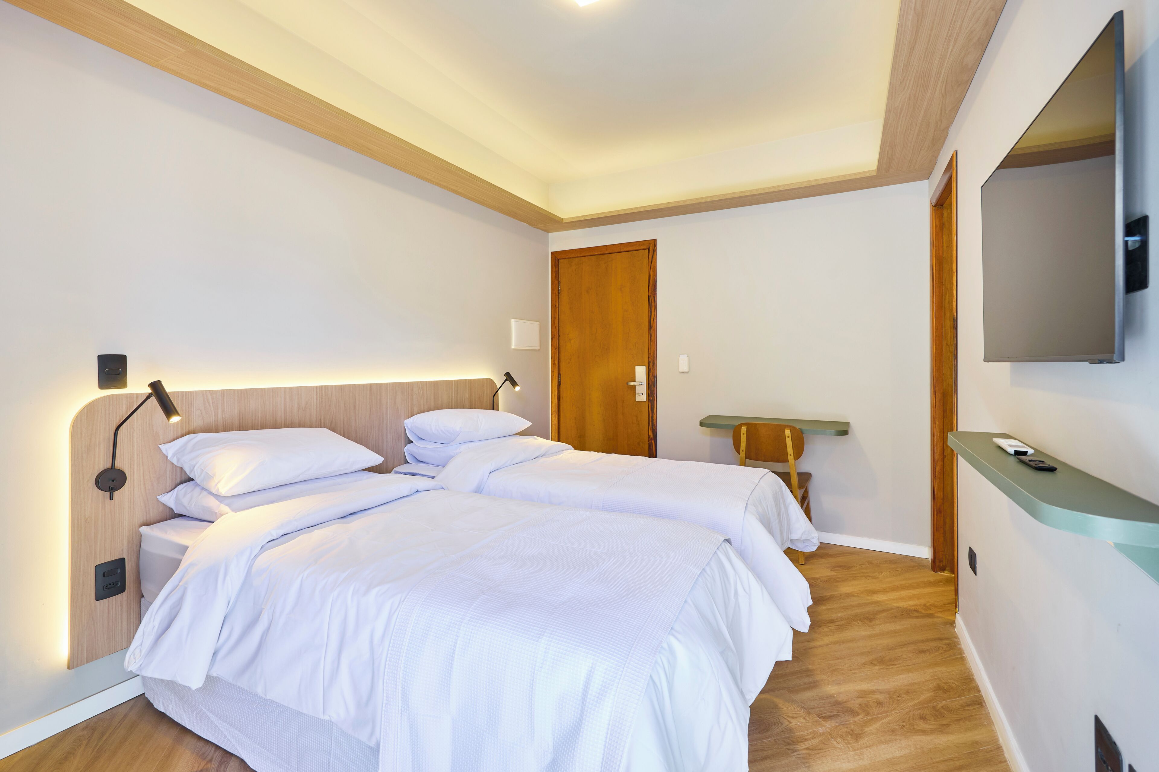 A modern hotel room with a large bed, bedside tables, a wooden ceiling, and a mounted TV.