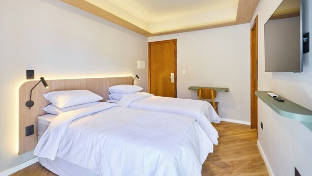A modern hotel room with a large bed, bedside tables, a wooden ceiling, and a mounted TV. - VILLA NK SUITES (Ubatuba)
