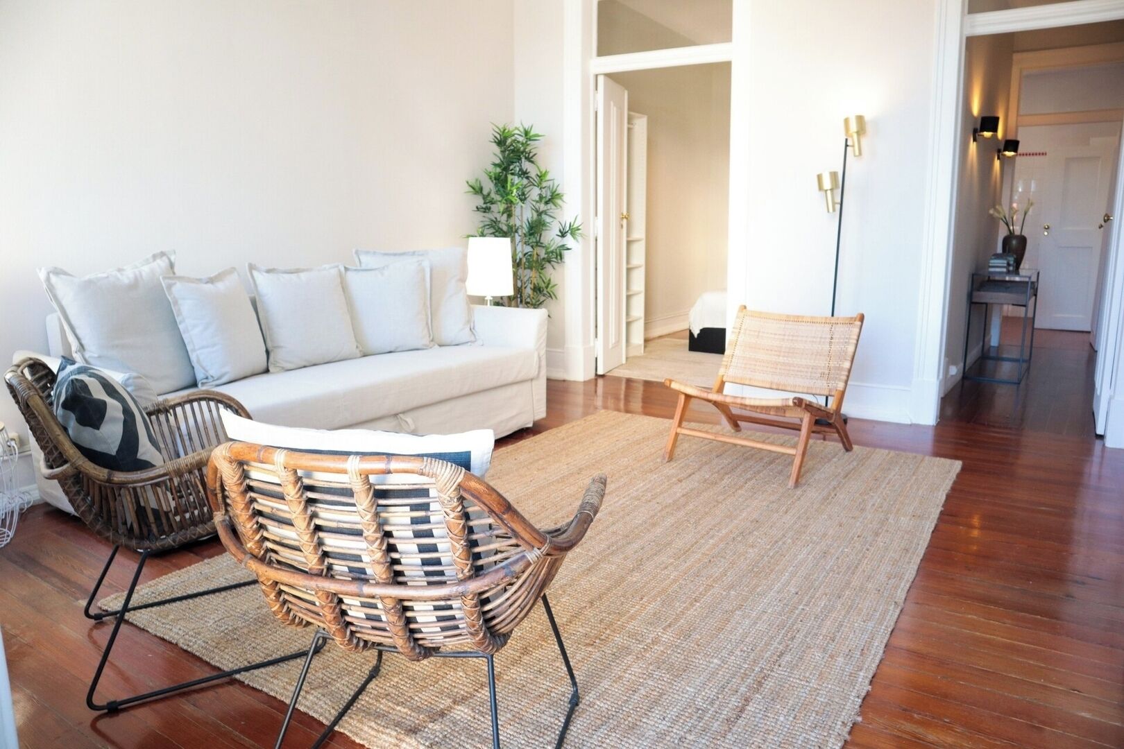 A living room with a sofa, two wicker chairs, a floor lamp, and a potted plant.