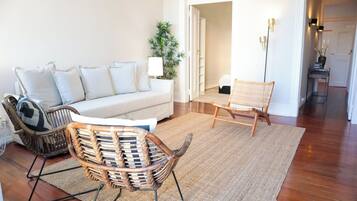A living room with a sofa, two wicker chairs, a floor lamp, and a potted plant.