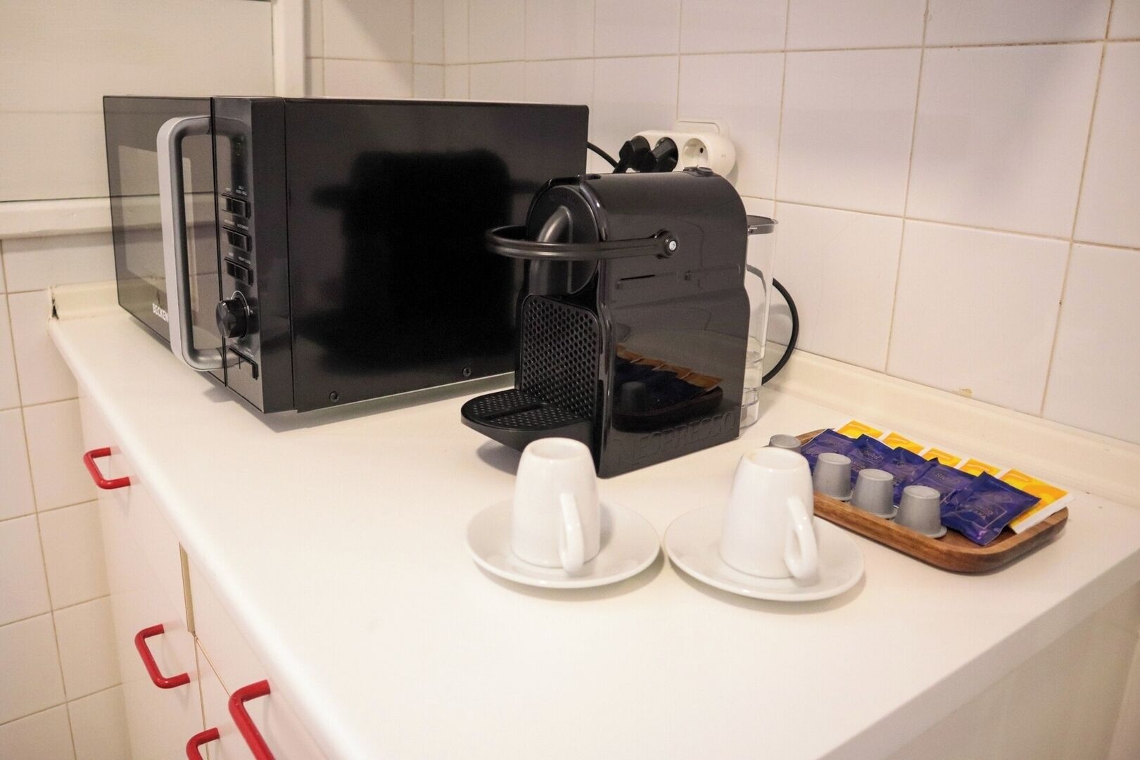 A kitchenette with a coffee maker, a toaster, and a tray with cups and coffee pods.
