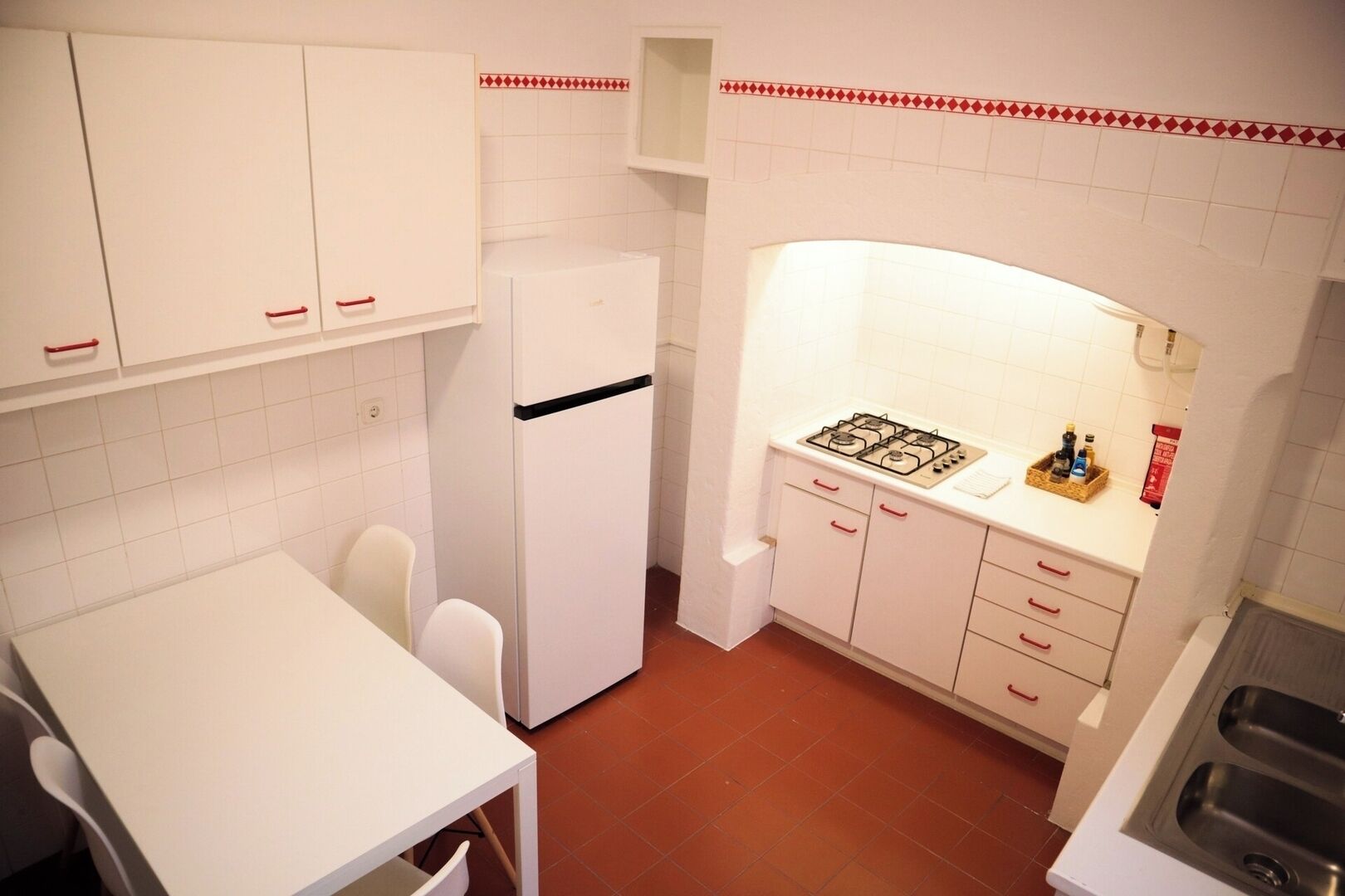 A compact kitchen with white cabinets, a white refrigerator, a gas stove, and a white table with two chairs.