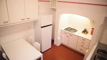 A compact kitchen with white cabinets, a white refrigerator, a gas stove, and a white table with two chairs.