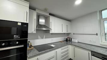 A modern kitchen with white cabinets, a stainless steel range hood, a built-in oven, and a window providing natural light.
