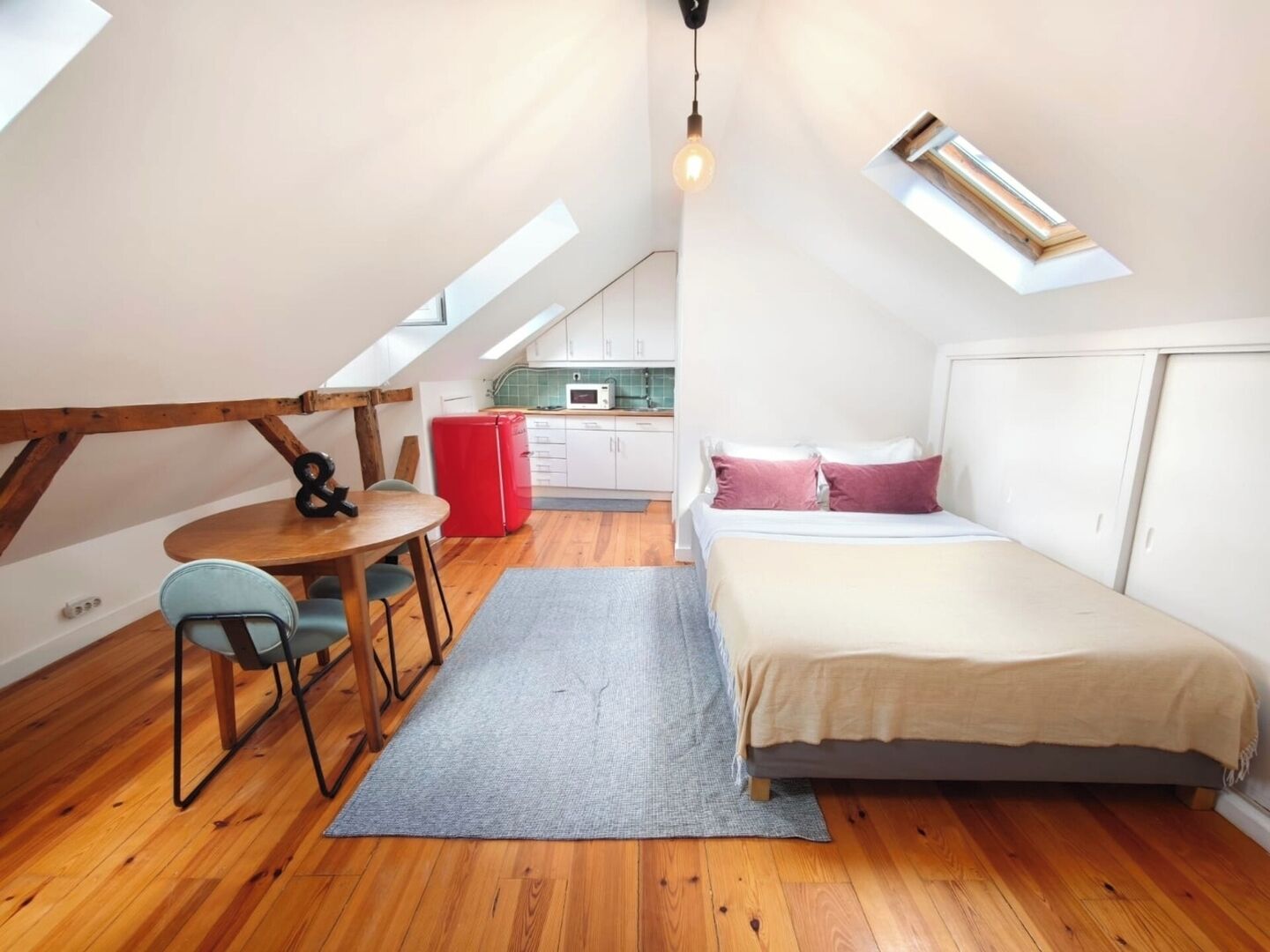 A compact room with a bed, a dining table, and a kitchenette.