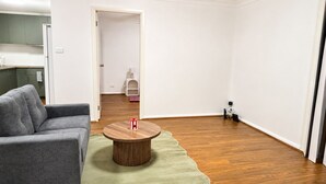 Een woonkamer met een grijze bank, een rond houten bijzettafeltje en een groen tapijt.