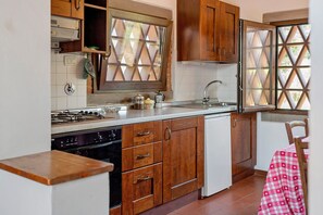 Una cocina con gabinetes de madera, estufa a gas, lavavajillas y ventana con persiana de diseño romboidal.
