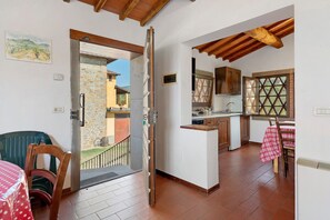 A kitchen with wooden cabinets, a dining area with a table and chairs, and a view of a garden through an open door.