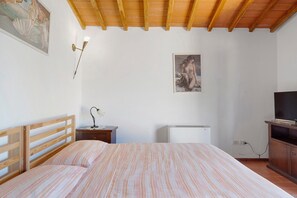 Un dormitorio con cama, mesita de noche, lámpara, cuadro y televisor.