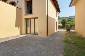 A building with a tiled patio, a glass door entrance, and a view of a green landscape.