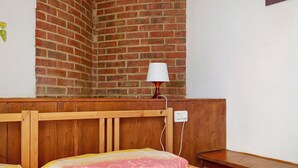 Une chambre avec un mur en briques, une tête de lit en bois, une table de chevet et un lit recouvert d’une couverture à motifs.