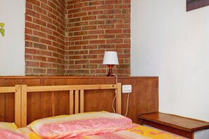 A room with a brick wall, a wooden headboard, a bedside table, and a bed with a patterned blanket. - Apartment 'Granaio' with Shared Garden, Wi-Fi and Air Conditioning (Terranuova Bracciolini)