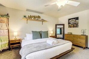 A hotel room with a bed, bedside tables, a dresser, a ceiling fan, a wall-mounted shelf with decorative items, and a painting. - Suncrest Rise! Family Escape Near Fort Carson (Colorado Springs)
