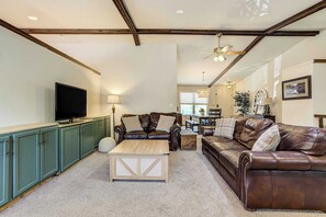 A spacious living room with a television, leather sofas, a coffee table, and a dining area in the background. - Suncrest Rise! Family Escape Near Fort Carson (Colorado Springs)