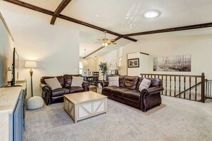A spacious living room with leather sofas, a wooden coffee table, and a staircase leading to an upper level. - Suncrest Rise! Family Escape Near Fort Carson (Colorado Springs)