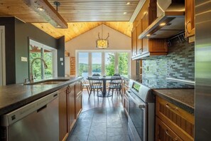 A modern kitchen with a central island, wooden cabinets, and a view of the outdoors. - La paix dans le Nord | Lac Brulé | SPA | SAUNA (Matawinie Regional County Municipality)