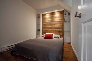 A bedroom with a wooden headboard, a bed with a grey blanket, and a red pillow. - La paix dans le Nord | Lac Brulé | SPA | SAUNA (Matawinie Regional County Municipality)
