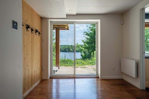 A room with a wooden wall, a sliding glass door leading to a lake view, and a white radiator. - La paix dans le Nord | Lac Brulé | SPA | SAUNA (Matawinie Regional County Municipality)