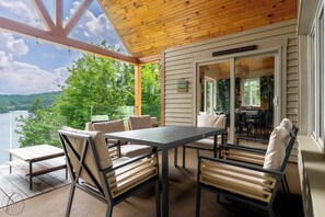 A covered outdoor seating area with a table and chairs, overlooking a body of water and greenery. - La paix dans le Nord | Lac Brulé | SPA | SAUNA (Matawinie Regional County Municipality)