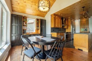 A modern kitchen with dark cabinets, a round dining table, and a wooden ceiling. - La paix dans le Nord | Lac Brulé | SPA | SAUNA (Matawinie Regional County Municipality)