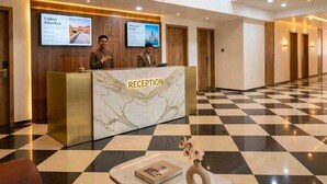 Zona de recepción de un hotel con mostrador, relojes y piso a cuadros.