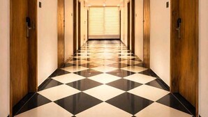 A hotel hallway with a checkered floor, wooden doors, and a ceiling light. - Fun Hotels Rajkot  (Rajkot)