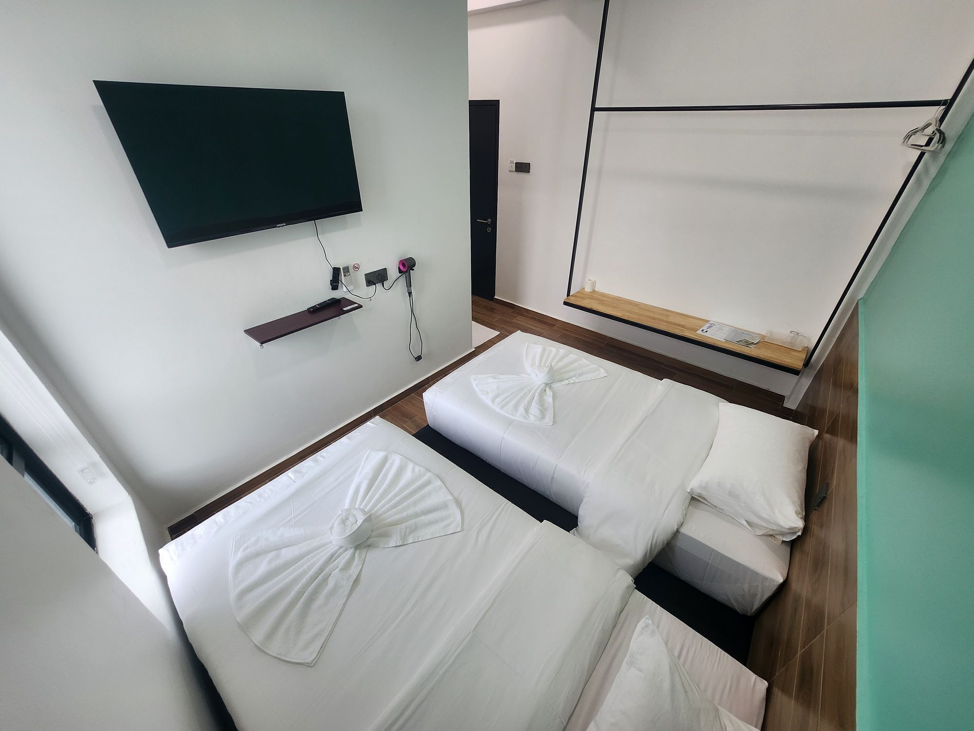 Habitación de hotel con dos camas, un televisor montado en la pared, un estante pequeño y suelo de madera.
