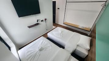 Habitación de hotel con dos camas, un televisor montado en la pared, un estante pequeño y suelo de madera.