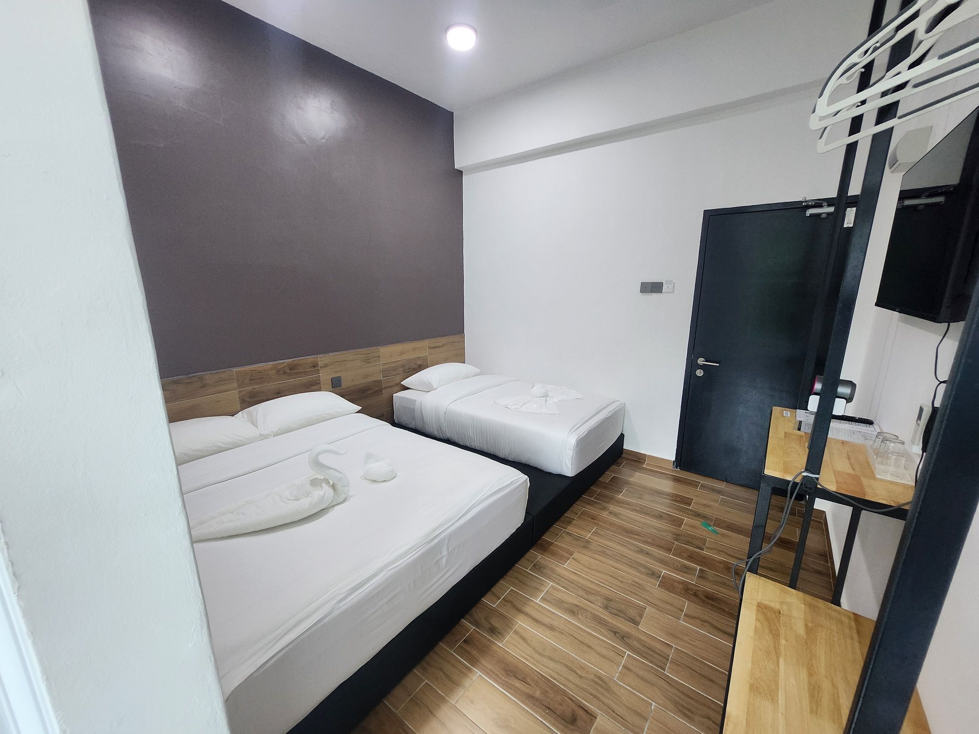 A hotel room with two beds, a wooden floor, a dark door, and a small desk with a chair.