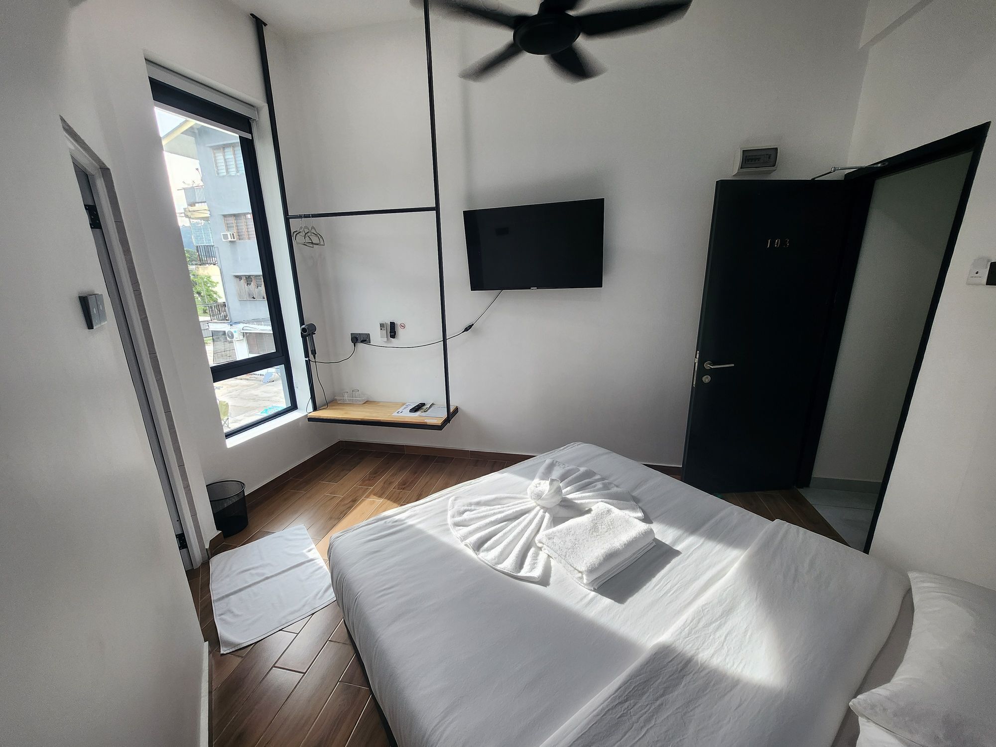 A hotel room with a bed, a ceiling fan, a TV mounted on the wall, and a window with a view of the outside.