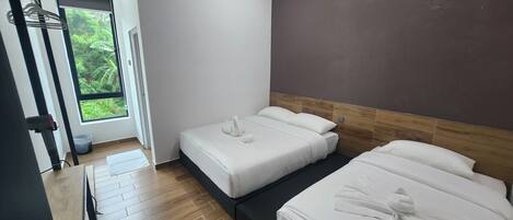 A hotel room with two beds, a window with a view of greenery, an air conditioning unit, and a wooden floor.