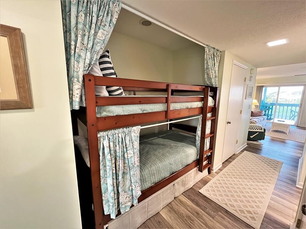 Una cama litera con estructura de madera, una cortina estampada y vistas a un balcón.