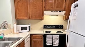Una cocina compacta con muebles de madera, un microondas, un horno y un refrigerador.