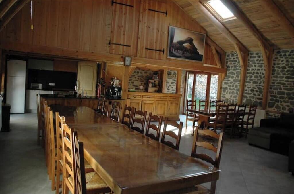 Un vaste espace dédié à la salle à manger, avec une longue table et des chaises en bois, un coin cuisine aux murs en pierre et une cheminée en pierre.