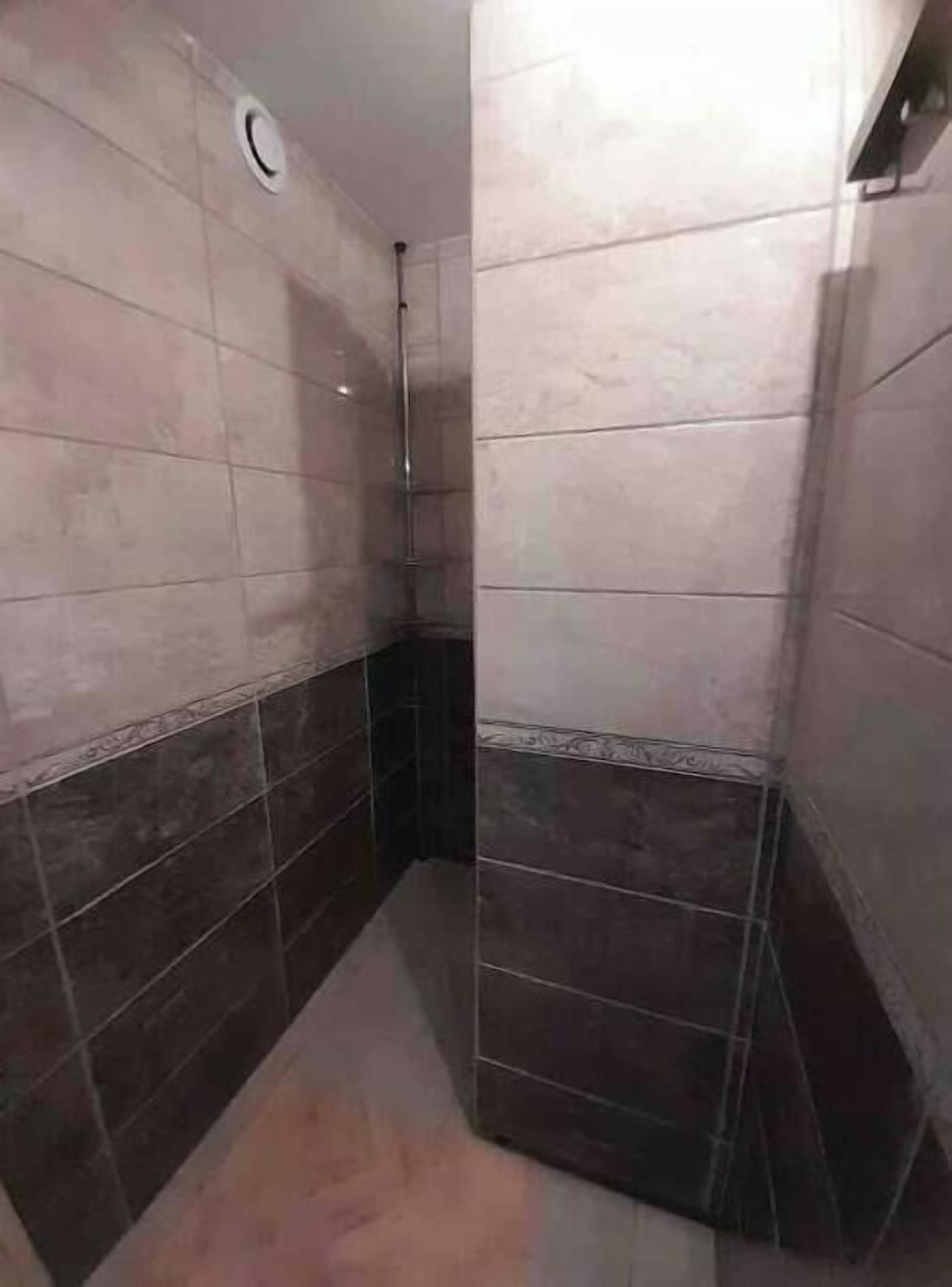 Een badkamer met betegelde wanden en vloer, een douchegedeelte en een toilet.