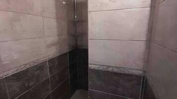 Een badkamer met betegelde wanden en vloer, een douchegedeelte en een toilet.