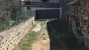 A narrow outdoor pathway flanked by stone walls, leading to a building with a dark door. - Charlie's house. (Le Monastier-sur-Gazeille)