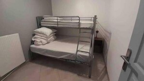 A bunk bed with a mattress and pillows, a radiator, and a door. - Charlie's house. (Le Monastier-sur-Gazeille)