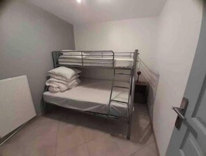 Uma cama box com colchão e almofadas, um radiador e uma porta.