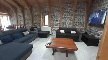 Een woonkamer met stenen muren, een houten plafond, een grote bank, een kleinere bank en een salontafel.