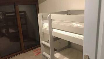 Een stapelbed met een onderbed en een deur naar een inloopkast met glazen schuifdeuren.